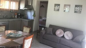 Una cocina moderna con una mesa de comedor y sillas, un sofá gris con cojines, y cuadros de flores en la pared.
