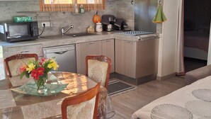 Cocina compacta con electrodomésticos modernos, zona de comedor con mesa y sillas, y entrada visible al baño.