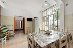 A dining area with a table, chairs, a television, and a window with a view. - Salento Short Let Apartment: Spacious, Bright, Private Terrace, Garden, Air Conditioning (Copertino)