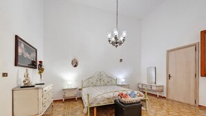 Um quarto com cama, penteadeira, cômoda, lustre e porta.