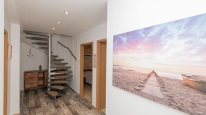 Eine Treppe mit Holzvertäfelung, eine Holztür und ein Gemälde mit Strandmotiv.