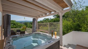Un bain à remous installé sous une pergola, offrant une vue sur la verdure et les montagnes.