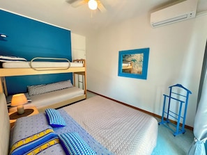 Ein Schlafzimmer mit Etagenbetten, einem Deckenventilator, einem kleinen Tisch mit Lampe, einem Bild an der Wand und einem blauen Stuhl.
