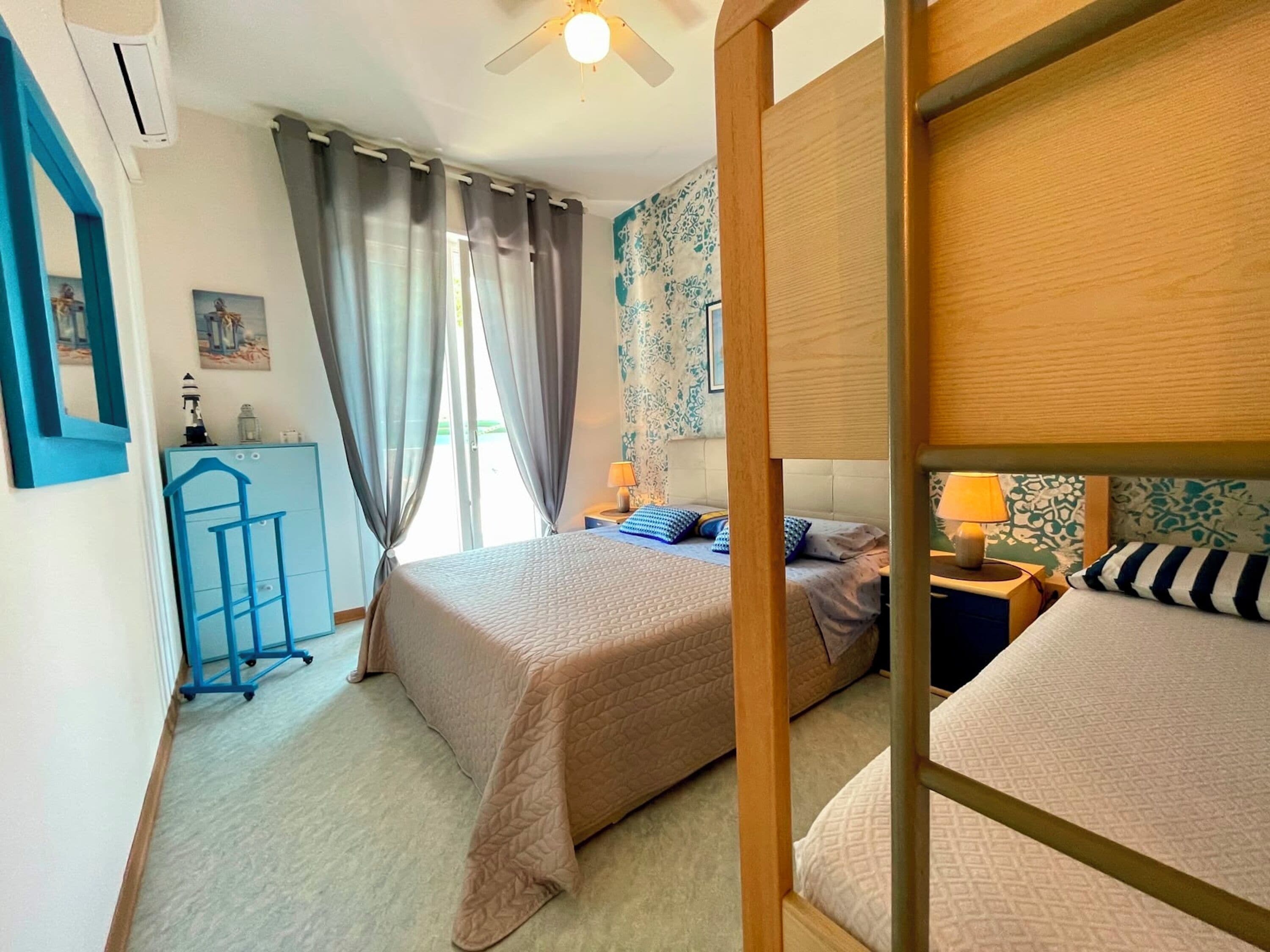 Un dormitorio con dos camas, un escritorio, una silla, un ventilador de techo y una ventana con cortinas.