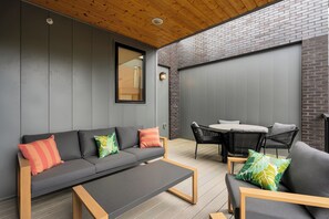 A modern outdoor living space with a grey sofa, wooden coffee table, and black wicker chairs. - The Grove (Nashville)