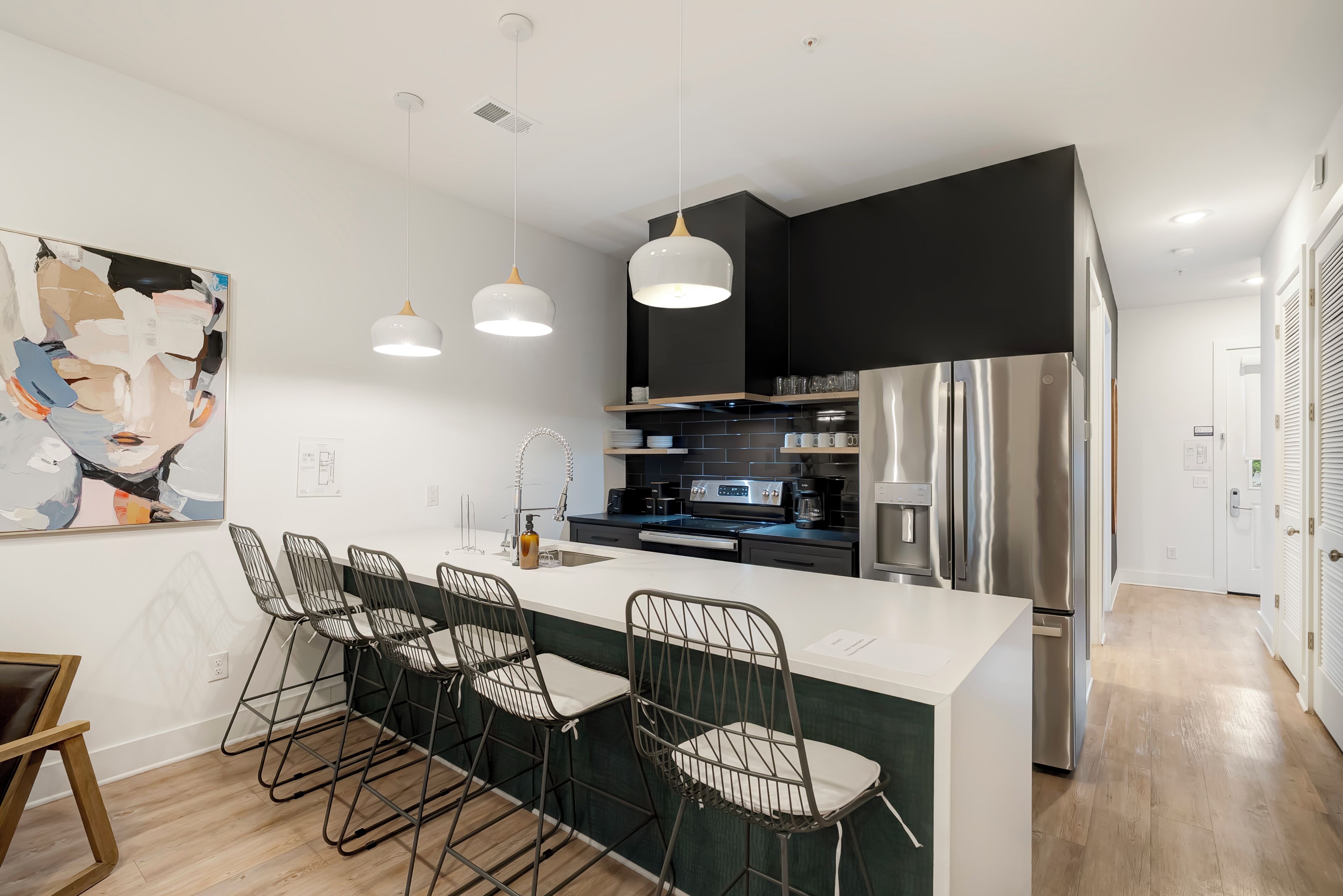 A modern kitchen with a central island, bar stools, pendant lights, and stainless steel appliances.