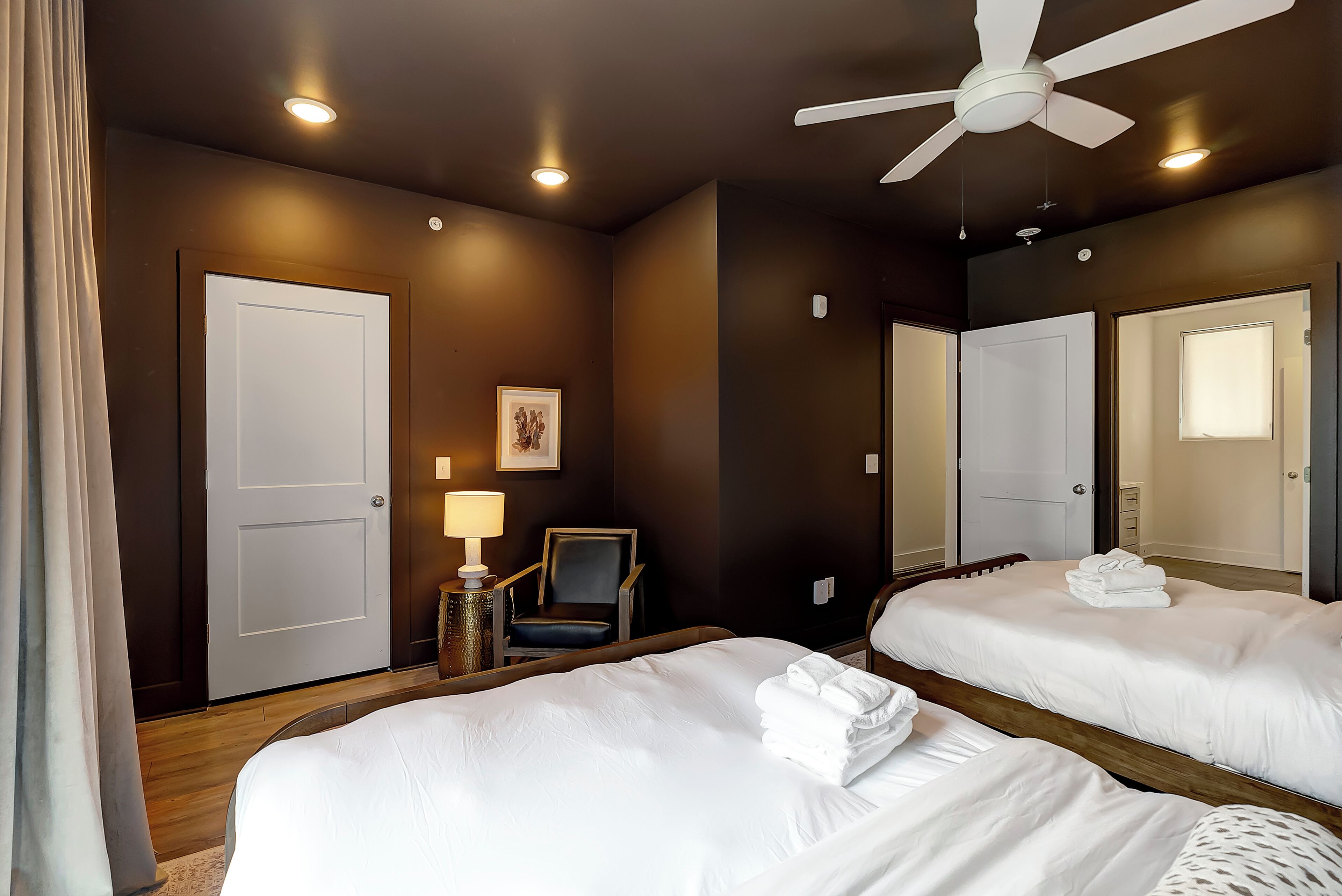 Habitación de hotel con una cama grande, una silla, un escritorio con lámpara, un ventilador de techo y un espejo.