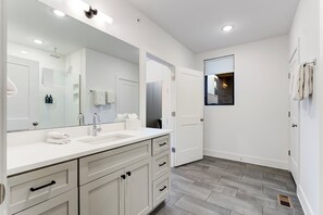 A modern bathroom with a large mirror, two sinks, and a shower area. - The Grove (Nashville)