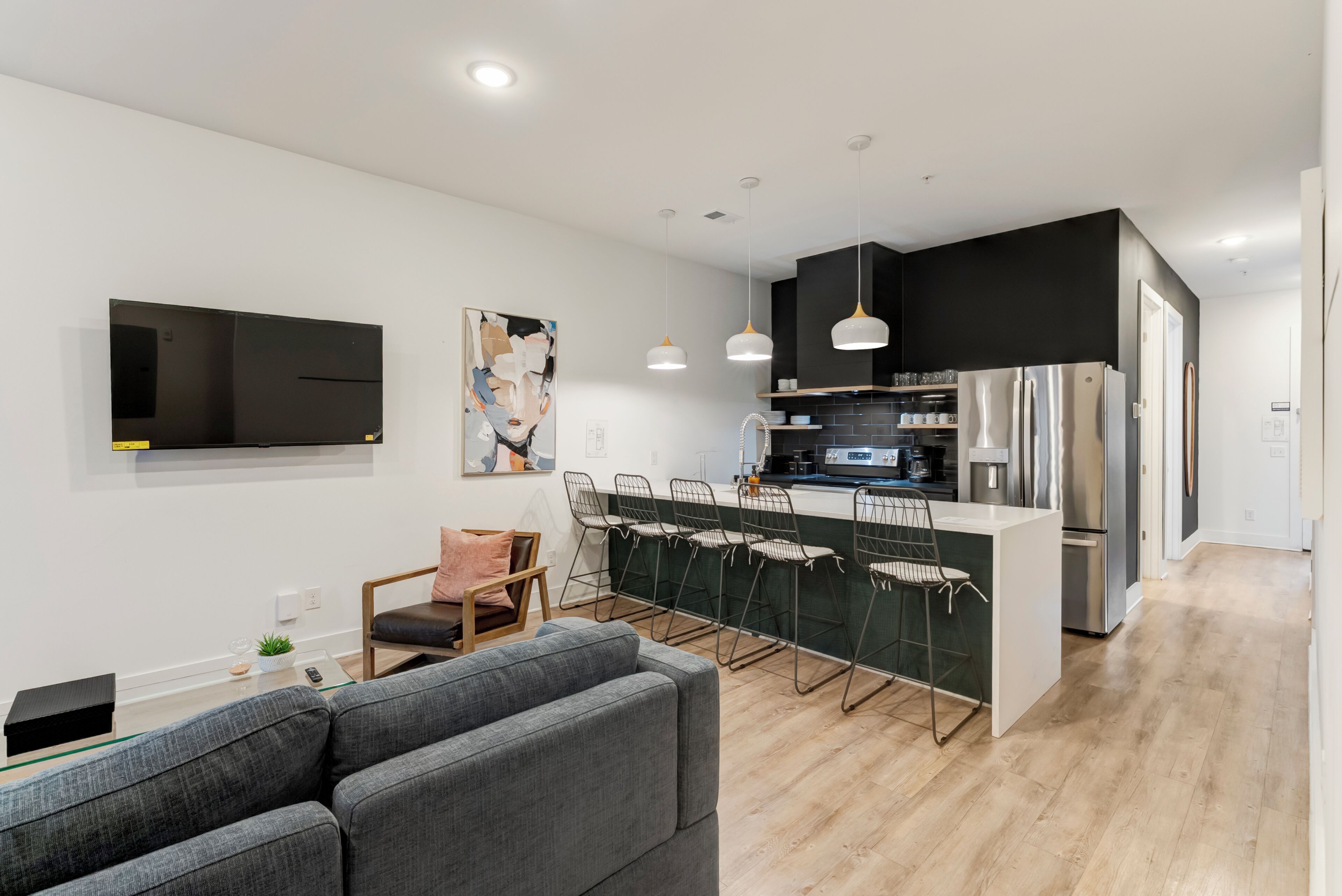 Una cocina moderna con una isla central, taburetes de bar, un televisor de pantalla plana y un comedor con sofá.