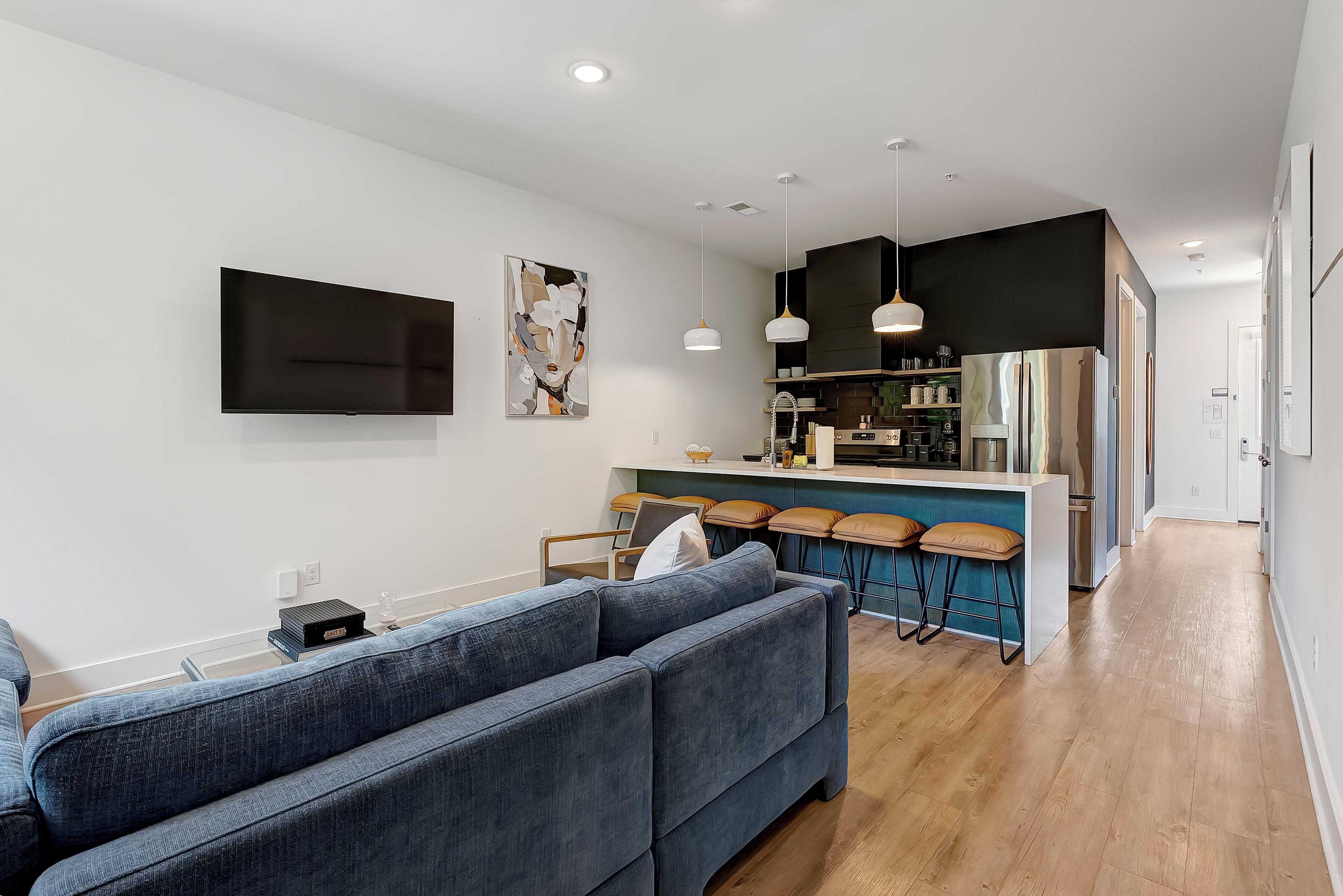 A modern living room with a sectional sofa, a flat-screen TV, and a kitchen area with bar stools.