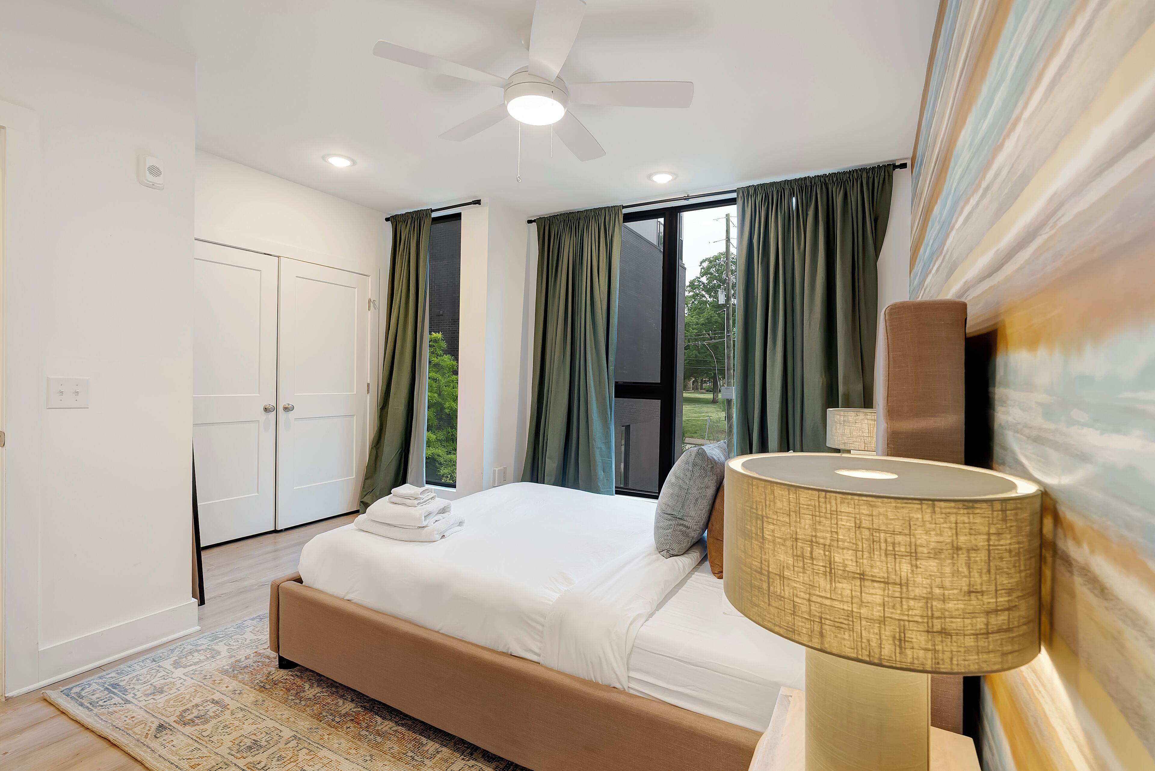 Une chambre à coucher avec un lit, un ventilateur de plafond, une fenêtre avec des rideaux et une lampe.