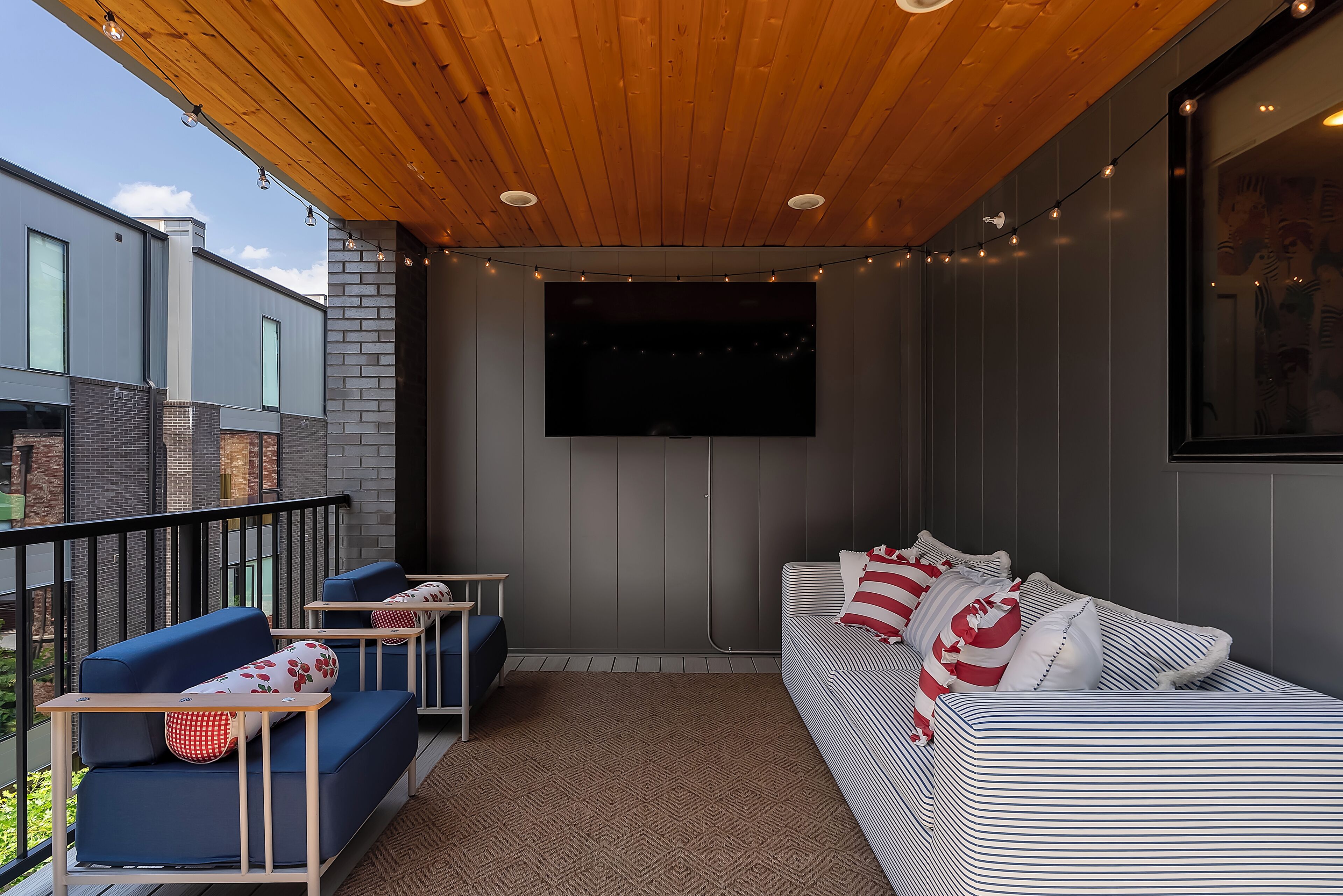 A modern outdoor seating area with a wooden ceiling, a flat-screen TV, and a patterned sofa.