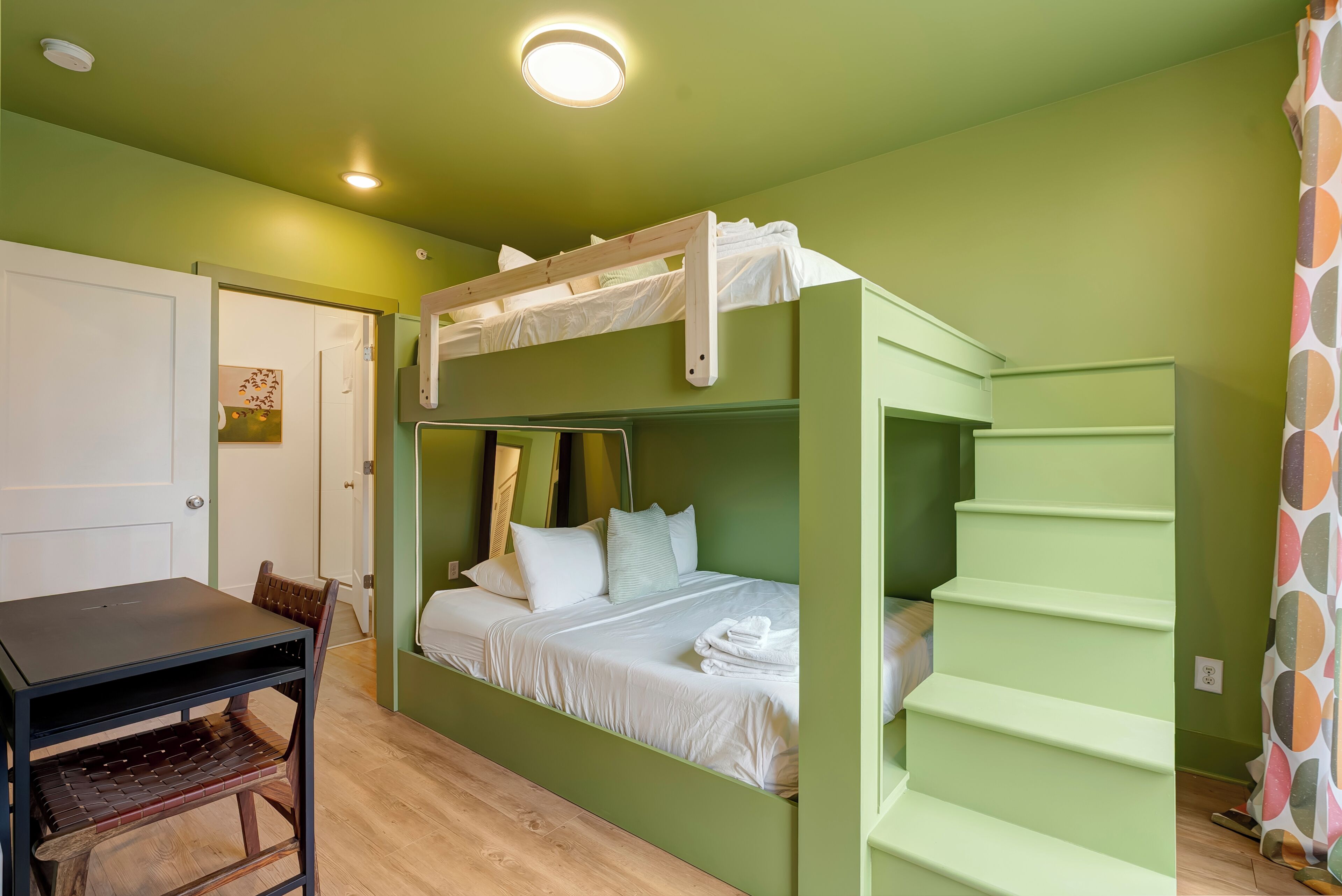 A bunk bed room with a desk and chair, a door, and a staircase.