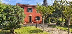 Una villa roja con un camino de piedra, rodeada de vegetación y árboles.