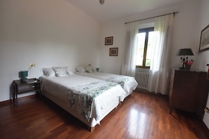 Un dormitorio con cama doble, mesita de noche con lámpara, cómoda y ventana con cortinas.