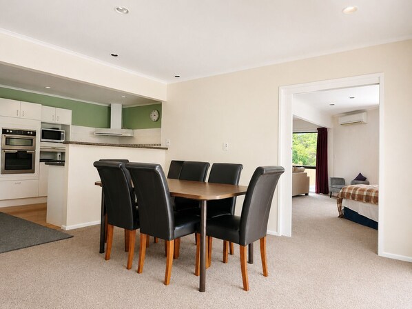 A modern kitchen with built-in appliances, a dining area with a wooden table and black chairs, and a view of a bedroom with a bed and a window.