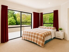 A bedroom with a large window, a bed with a plaid bedspread, a nightstand, and a potted plant.