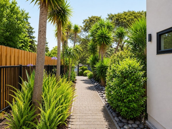 A paved pathway flanked by lush greenery and a wooden fence.