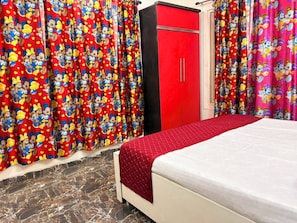 Une chambre à coucher avec un lit, des rideaux rouges ornés de personnages de dessins animés, une armoire rouge et un sol en marbre.