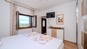 Une chambre à coucher avec un lit, une télévision, un bureau et une fenêtre avec des rideaux.