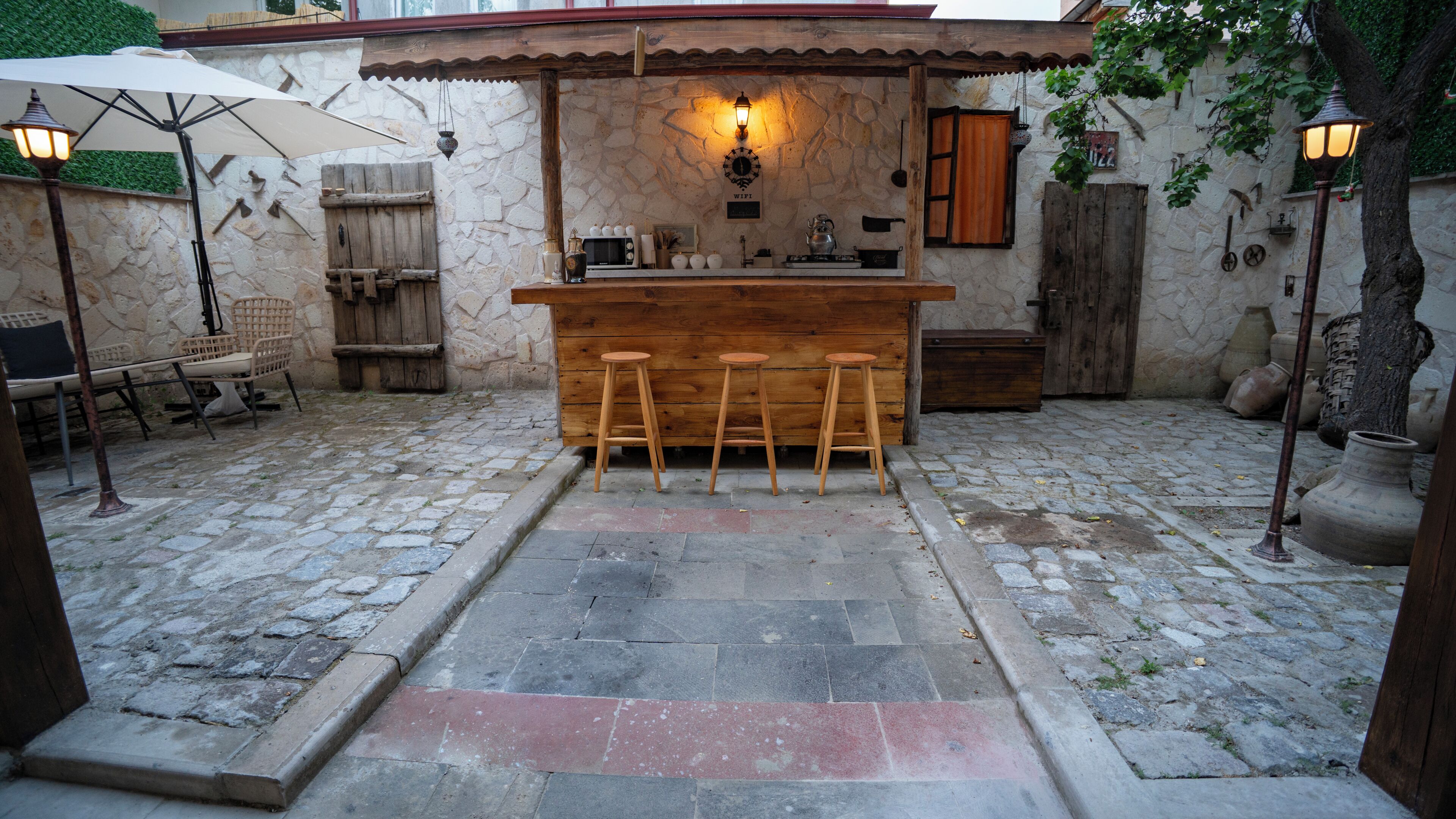 Un área de bar al aire libre de estilo rústico, con suelo de piedra, taburetes de madera y un muro de piedra de fondo.