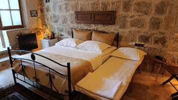 Una habitación con pared de piedra, una cama con ropa blanca, una mesita de noche, un radiador y una ventana.