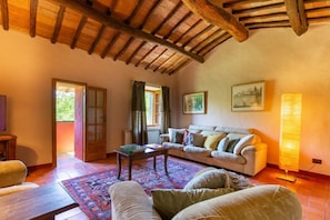 A cozy living room with a wooden ceiling, a sofa, a coffee table, and a lamp. -  Chianti country retreat 10 pax (Radda in Chianti)