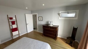 A bedroom with a bed, wooden dresser, chair, and a ladder with towels.