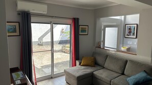 A modern living room with a sliding glass door leading to an outdoor area, a grey sofa with cushions, and framed artwork on the walls. - Modern apartment with a terrace in the heart of town (Vila Franca Do Campo)