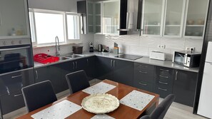 A modern kitchen with dark cabinets, a wooden dining table, and a built-in oven. - Modern apartment with a terrace in the heart of town (Vila Franca Do Campo)