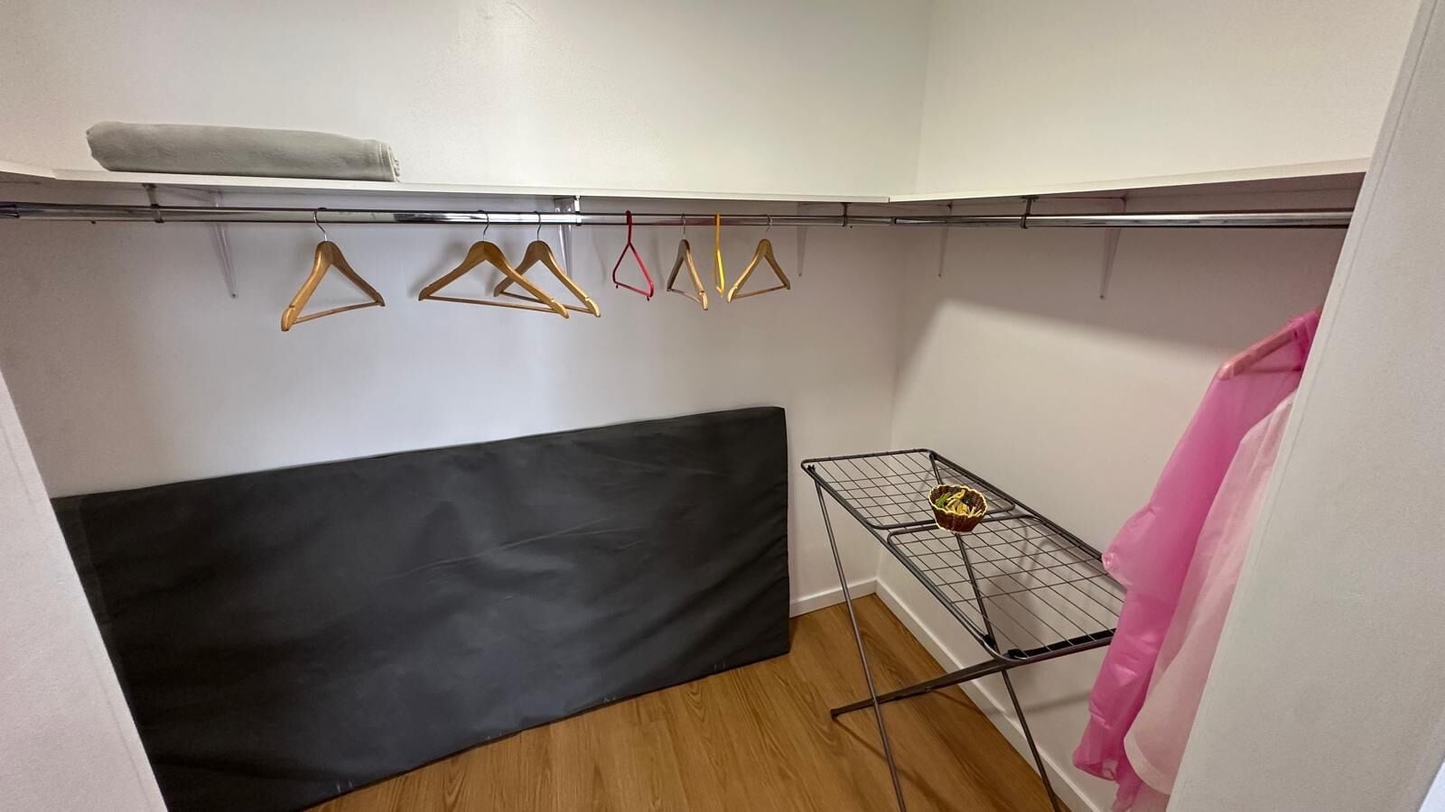 A small room with a black sofa, a metal drying rack with clothes, and a white wall.