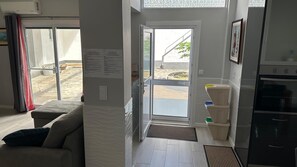 Ein Wohnzimmer mit einer Couch, einer Glastür zum Außenbereich, einer Küche mit Kühlschrank und einer Wand-Klimaanlage.