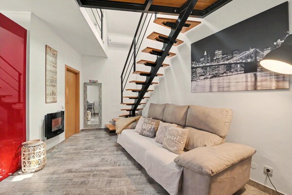 A modern interior with a staircase, a sofa, and a cityscape painting.