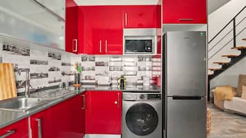 A modern kitchen with red cabinetry, stainless steel appliances, and a tiled backsplash.