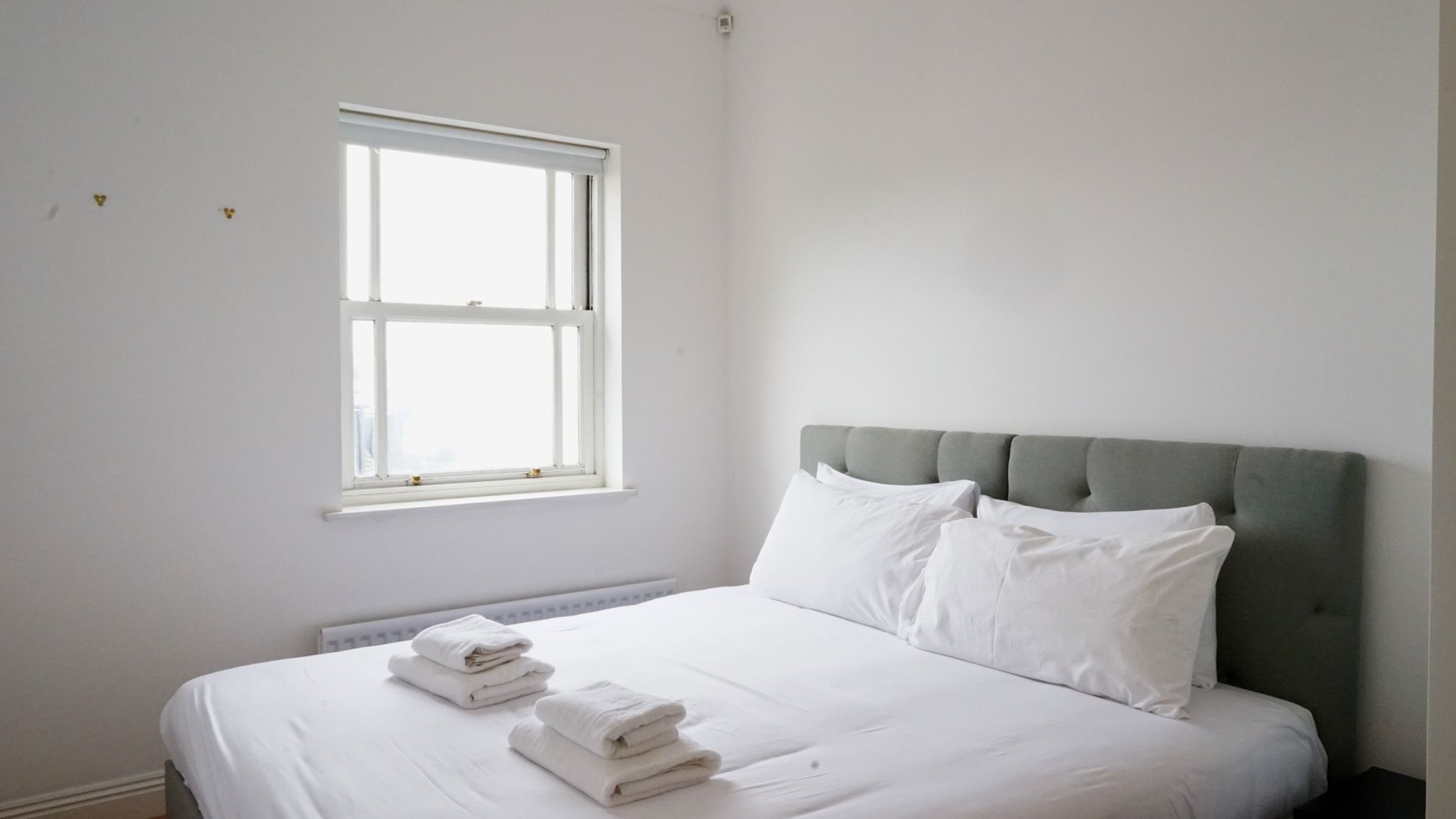 Een slaapkamer met een bed, kussens, een raam en handdoeken.