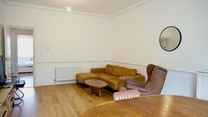 Une pièce avec un plancher en bois, un canapé marron, une table ronde, une chaise, un radiateur, un téléviseur et un miroir au mur.