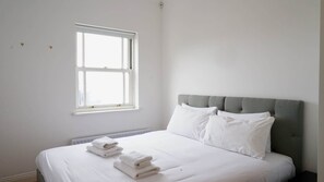 A bedroom with a bed, pillows, a window, and a radiator. - Light Filled 2BDR Riverside Retreat Rotherhithe (London)