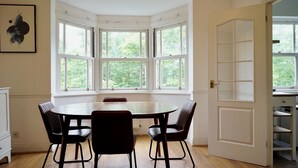 Une pièce dotée d’une baie vitrée, d’une table ronde entourée de chaises et d’une porte blanche.