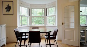 A room with a bay window, a round table with chairs, and a white door. - Light Filled 2BDR Riverside Retreat Rotherhithe (London)