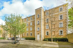 A multi-story residential building with a brick facade, a central entrance, and a paved courtyard with a bicycle parked outside. - Light Filled 2BDR Riverside Retreat Rotherhithe (London)