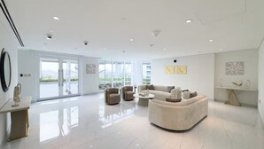 A spacious, modern living room with a large, curved sofa, a coffee table, and two armchairs. A large window provides a view of the outdoors. - Vogue | Skyz by Danube near Dubai Miracle Garden (Dubai)