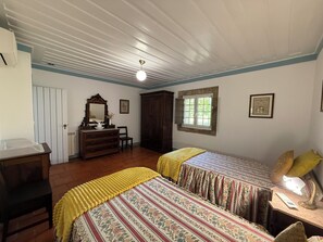 Une chambre avec deux lits, une commode, un miroir, une fenêtre et un ventilateur de plafond.