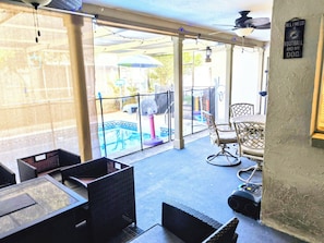 Un espacio de patio techado con mobiliario exterior, piscina y ventilador de techo.