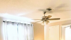 A bedroom with a bed, a ceiling fan, a nightstand, a dresser, and a window with curtains.