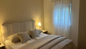 Une chambre d’hôtel avec un lit, une table de chevet, une lampe et une fenêtre avec des rideaux légers.