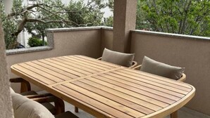 Une table en bois, des chaises et des coussins sur un balcon extérieur.