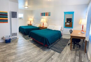 Habitación de hotel con dos camas, un escritorio, una silla, un televisor y un espejo.