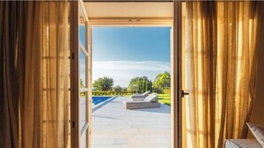 Une porte ouverte donnant sur un patio avec une piscine, du mobilier d’extérieur et un ciel dégagé.