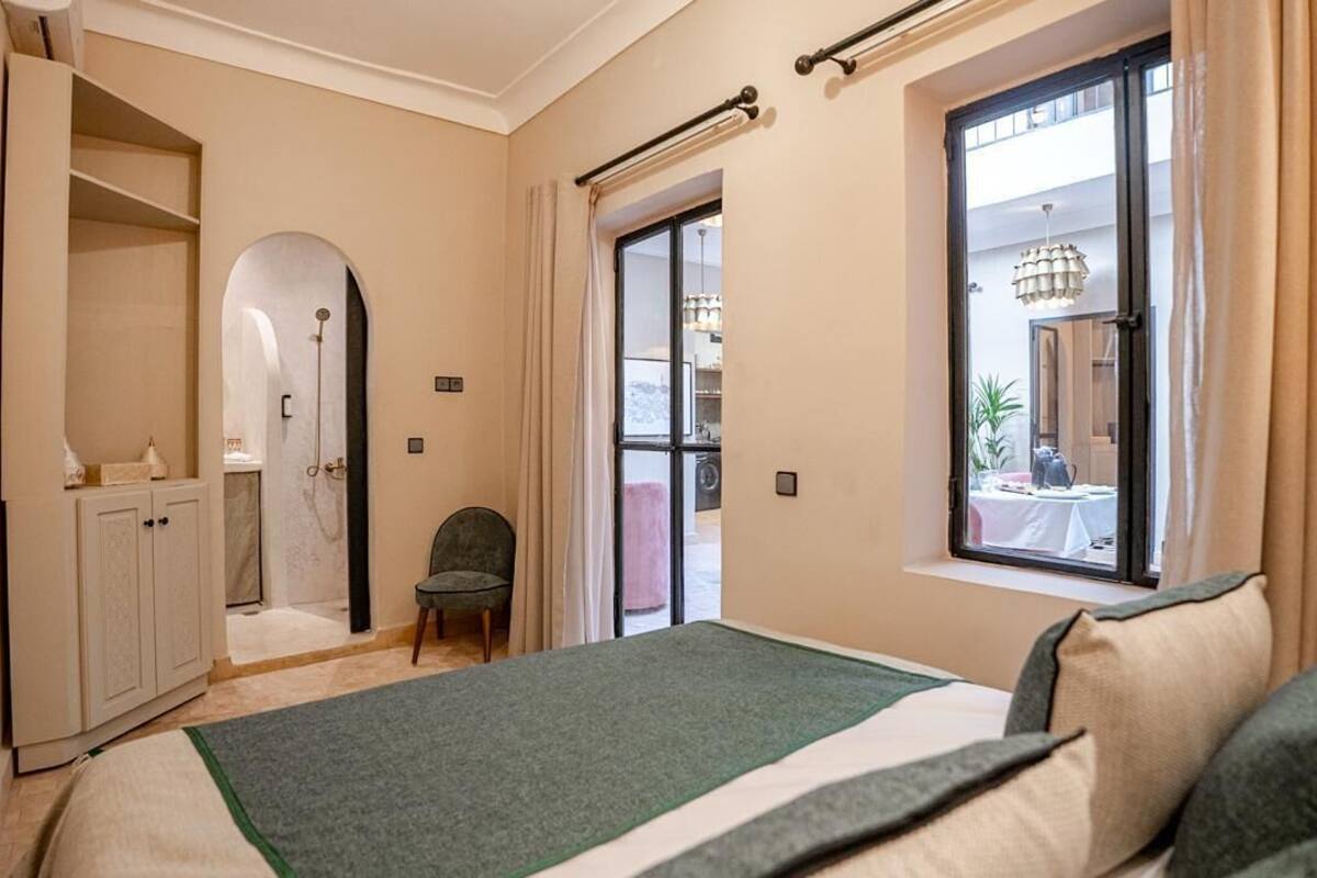 A bedroom with a bed, a wardrobe, a chair, a window with curtains, and a view of the outside.