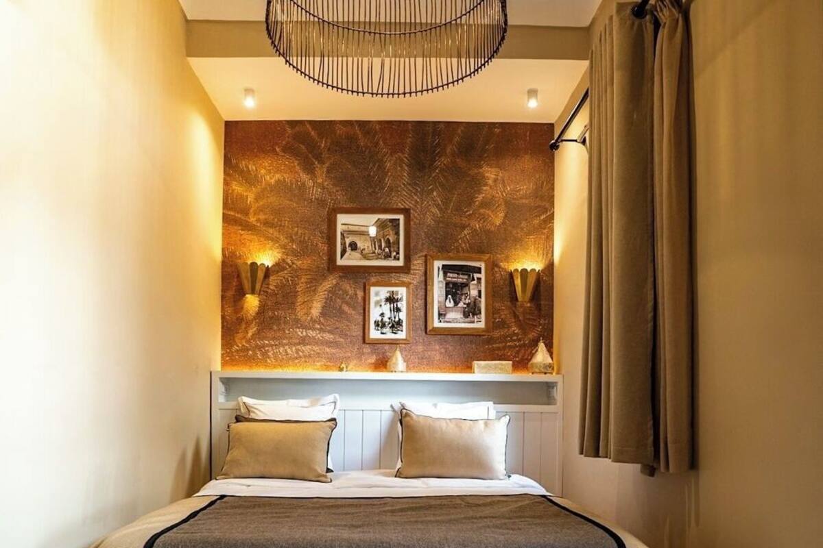 A bedroom with a bed, a wall-mounted light fixture, and framed pictures.